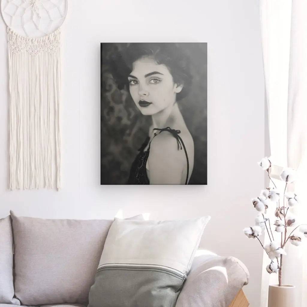 Un Tableau Femme Vintage Portrait Noir et Blanc présente une femme aux cheveux courts, ornant un mur blanc au-dessus d'un canapé gris avec un coussin beige. Le décor respire l'élégance intemporelle, sublimé par un attrape-rêves et un vase à tiges de coton.