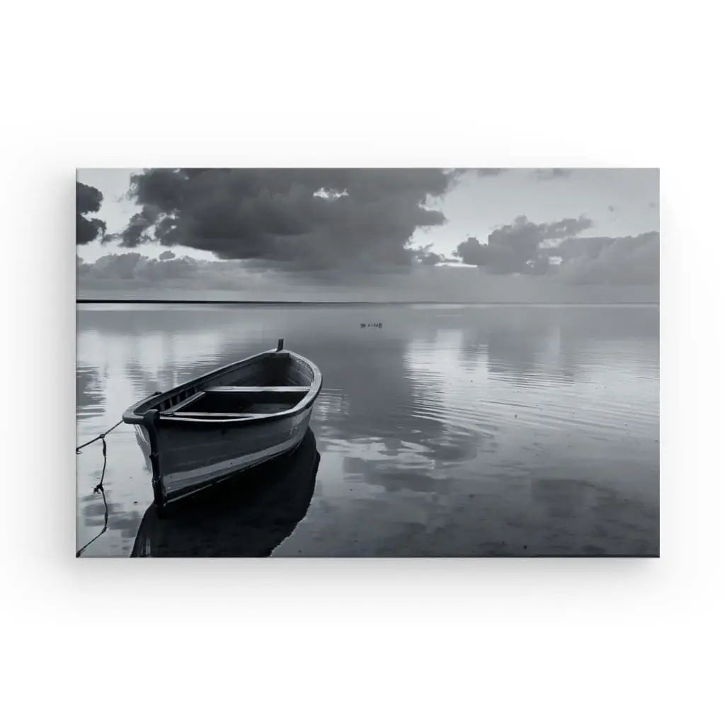 Une barque solitaire est amarrée dans une eau calme sous un ciel nuageux. Le Tableau Barque Lac Paisible Noir et Blanc capture une scène sereine et réfléchie.