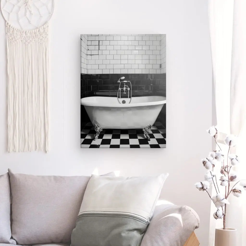 Un Tableau Salle de Bain Baignoire Noir et Blanc encadré est accroché sur un mur blanc au-dessus d'un canapé gris clair, à côté d'une tenture murale en macramé et d'un cotonnier en pot, créant un élégant tableau noir et blanc.