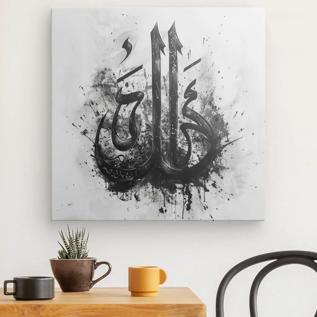 Une toile avec l'art de la calligraphie arabe, "Tableau Allah Ecriture Noir et Blanc", à l'encre noire sur fond blanc, est suspendue comme décoration spirituelle au-dessus d'une table en bois avec deux tasses et une petite plante en pot.