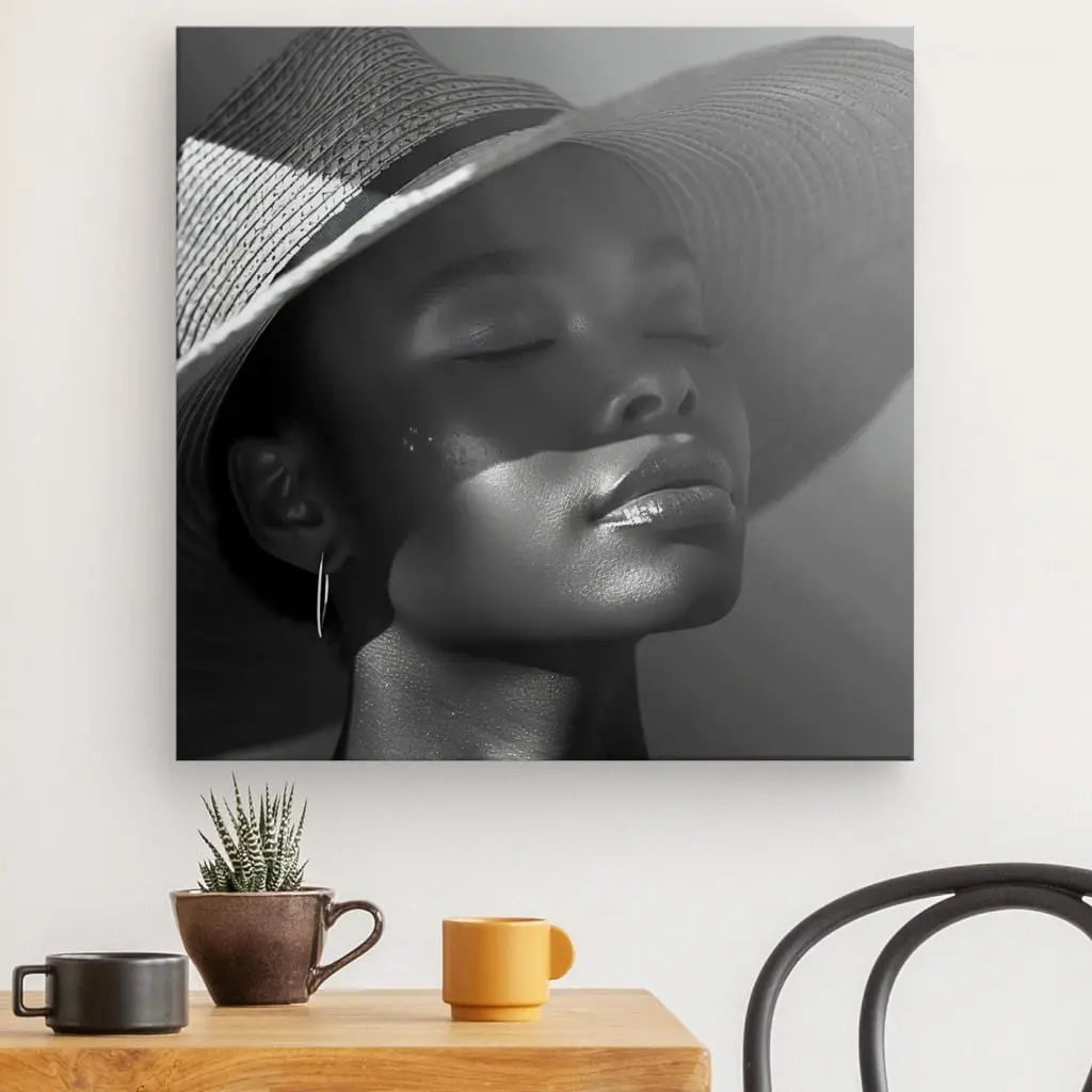 Une photographie en noir et blanc intitulée « Tableau Portrait Femme Chapeau Soleil Noir et Blanc » d'une personne portant un Chapeau Soleil est exposée sur un mur au-dessus d'une table en bois avec une plante et deux tasses.