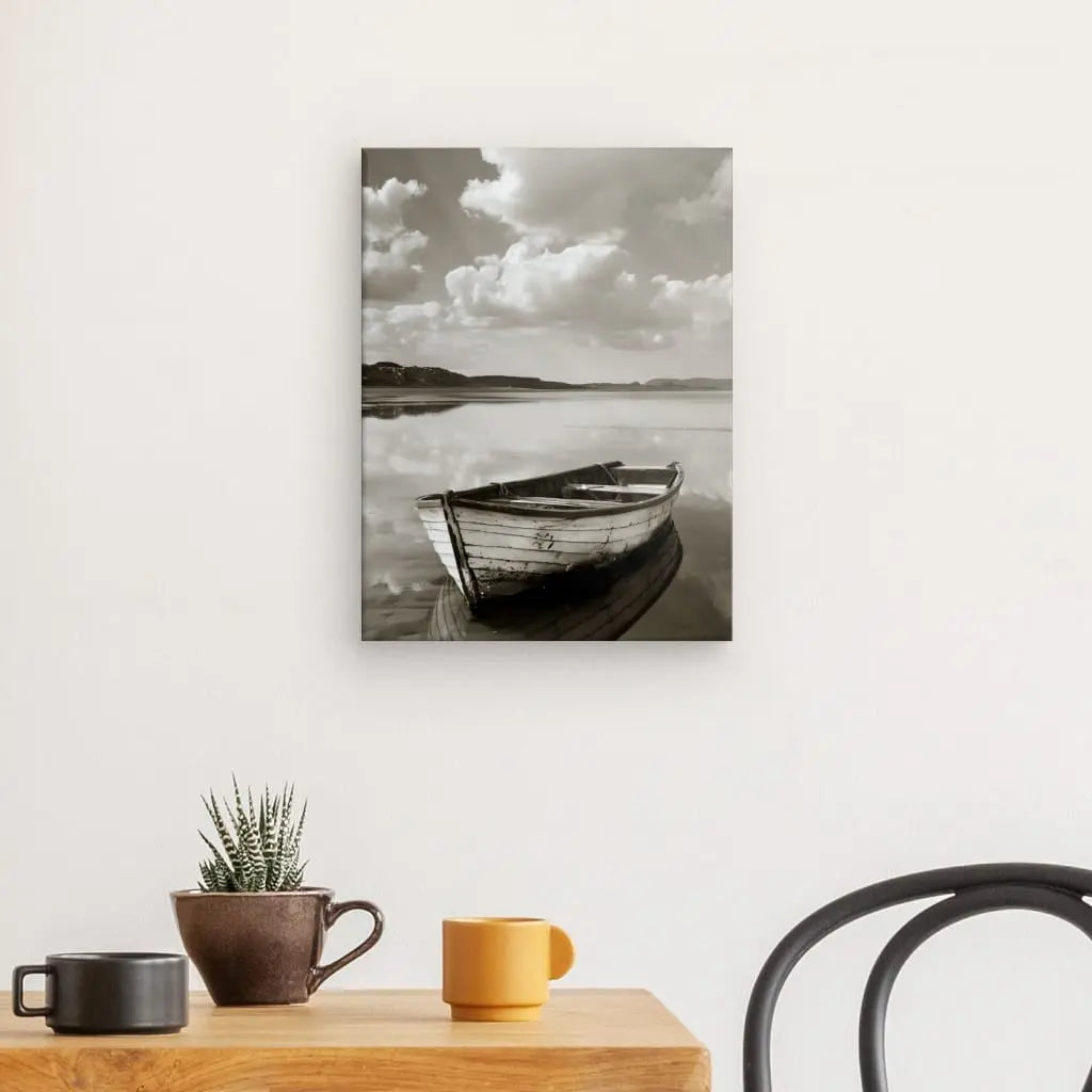 Un Tableau Bateau Lac Noir et Blanc Sépia représentant un navire en bois sur des eaux calmes est élégamment accroché à un mur blanc au-dessus d'une table ornée d'une petite plante en pot et de deux tasses, créant un décor artistique.