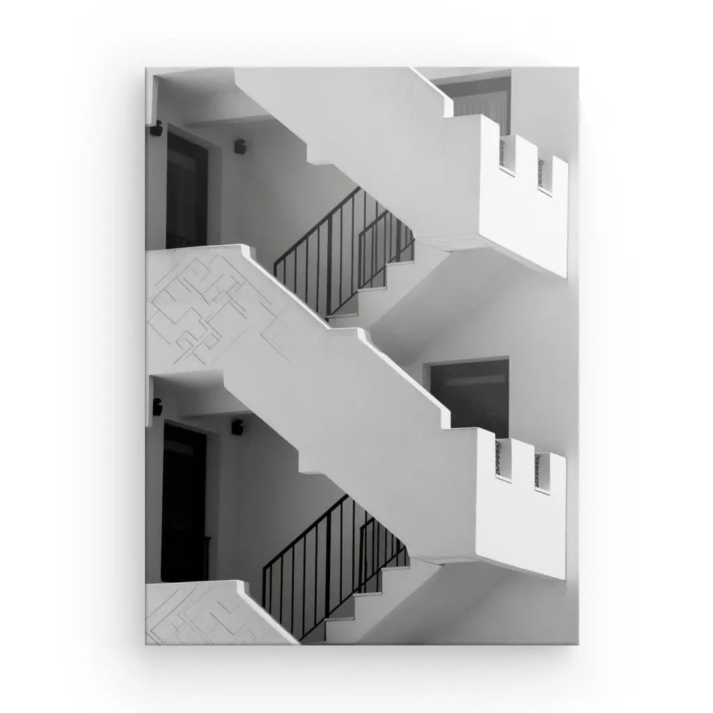 Une photo en niveaux de gris représentant un escalier minimaliste à trois niveaux, des rampes noires et des murs d'un blanc éclatant. La conception comprend des motifs géométriques et des cadres de portes rectangulaires, mettant en valeur l’exquis Tableau Escaliers Noir et Blanc Paysage Architectural.