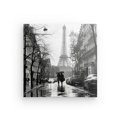 Photographie en noir et blanc d'une rue pluvieuse de Paris, avec des gens tenant des parapluies et la Tour Eiffel visible en arrière-plan, capturant l'essence du Tableau Paris Tour Eiffel Photo Rue Noir et Blanc.