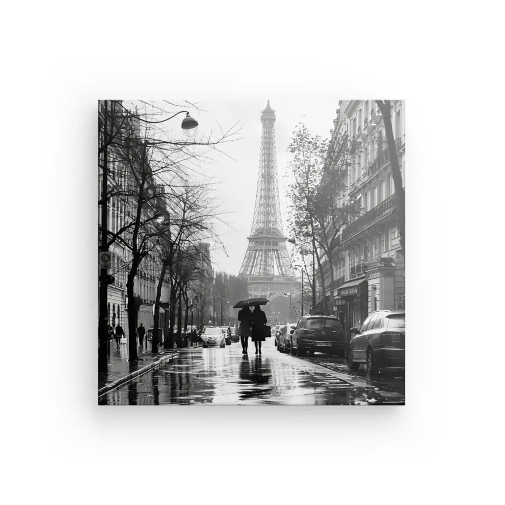Photo en noir et blanc d'une scène de rue pluvieuse à Paris avec la Tour Eiffel en arrière-plan. Deux personnes munies de parapluies déambulent dans les rues parisiennes, flanquées d'immeubles et de voitures garées des deux côtés. Il s'agit du Tableau Paris Tour Eiffel Photo Rue Noir et Blanc.