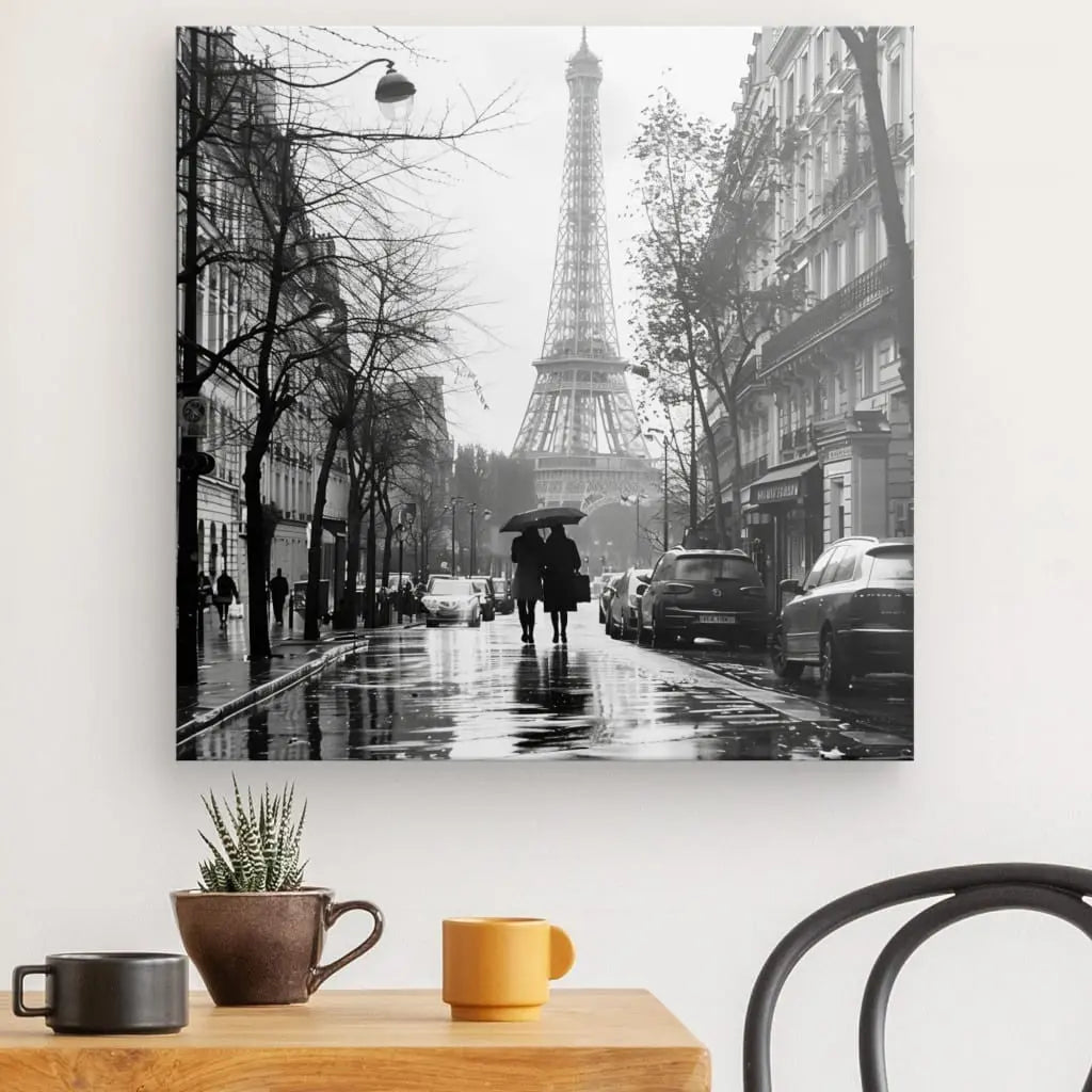Le Tableau Paris Tour Eiffel Photo Rue Noir et Blanc capture deux personnes avec un parapluie marchant dans une rue mouillée en direction de la Tour Eiffel à Paris, entourées de rues parisiennes bordées d'immeubles et de voitures garées.
