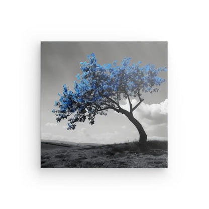 Un arbre aux feuilles bleues, ou *Tableau Campagne Monochrome Arbre Feuilles Bleues*, se dresse seul sur une colline sur fond de tableau monochrome, sous un ciel partiellement nuageux.