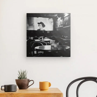 Une table en bois avec des tasses et une plante en pot se trouve devant un mur blanc affichant un Tableau Cinéma Classique Scène Noir et Blanc, créant une scène noir et blanc dans un décor intérieur.