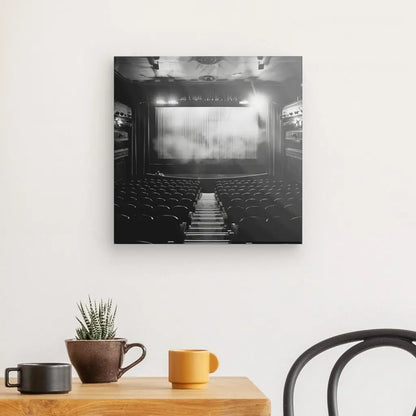 Un Tableau Théâtre Vide Scène Rétro Noir et Blanc est exposé sur un mur blanc au-dessus d'une table en bois avec une plante en pot, une tasse jaune et une tasse marron. Une chaise noire est partiellement visible.