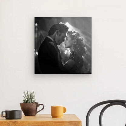 Un Tableau Scène Amour Baiser Noir et Blanc d'un couple romantique dansant, accroché sur un mur blanc au-dessus d'une table en bois avec une petite plante, une tasse et une tasse.