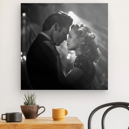 Un *Tableau Scène Amour Baiser Noir et Blanc* capture un homme et une femme se faisant face, leurs têtes se touchant dans un moment intime. Une tasse à café, une plante et une chaise sont visibles au premier plan, ajoutant de la profondeur à cette scène artistique romantique.