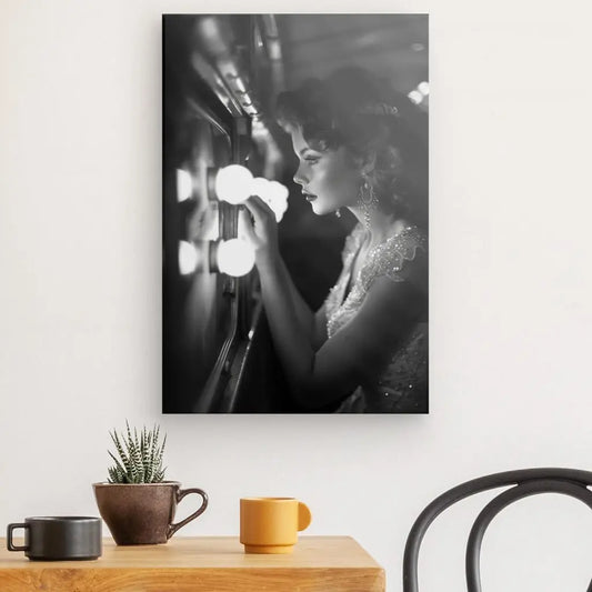 Photo en noir et blanc d'une femme regardant dans un miroir de courtoisie éclairé, montée sur un mur blanc au-dessus d'une table avec deux tasses et une petite plante en pot. La scène dégage un charme vintage de décoration, qui rappelle une époque d’illustration noir et blanc. Tableau Pin up Femme Rétro Noir et Blanc.