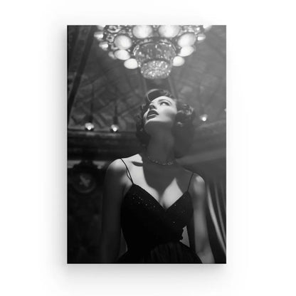 Photo en noir et blanc d'une femme vêtue d'une robe sombre levant les yeux, debout sous un lustre dans un décor richement décoré, évoquant l'essence du Luxe Noir et Blanc de Tableau Portrait Diva Femme des années 50.