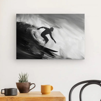 Un Tableau Surfeur Vague Rouleau Noir et Blanc capture l'essence d'un surfeur chevauchant une vague, accroché sur un mur blanc au-dessus d'une table en bois avec une plante en pot et deux tasses. Une chaise est partiellement visible à droite.