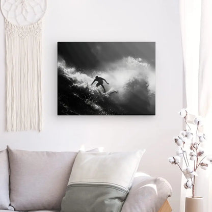Un salon avec un canapé blanc, des coussins, un Tableau Surf Océan Noir et Blanc mural présentant une photo monochrome d'un surfeur intrépide chevauchant une vague océanique, une tenture murale en macramé et un vase avec des tiges de coton sur une table d'appoint.