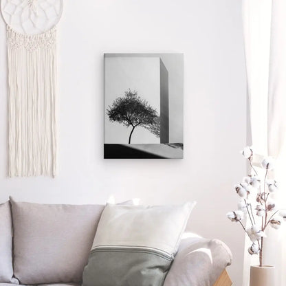 Un salon minimaliste comprend un canapé gris avec des oreillers blancs et gris, un tableau Architecture Naturelle Arbre Noir et Blanc, une tenture murale en macramé et un vase avec des tiges de coton blanc. La décoration intérieure soignée équilibre parfaitement l'esthétique moderne et le confort douillet.