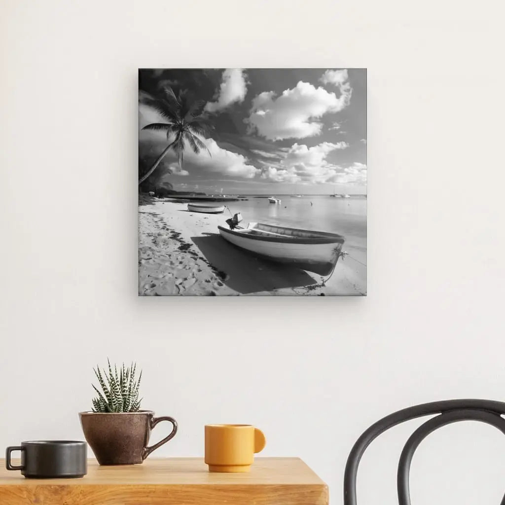 Une photo en noir et blanc d'une plage tropicale avec des bateaux et des palmiers, évoquant un Tableau Plage Cocotier Bateau Ile Noir et Blanc, est affichée sur un mur blanc. En dessous se trouve une table en bois avec deux tasses, une plante et une chaise.