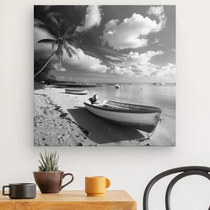 Un Tableau Plage Cocotier Bateau Ile Noir et Blanc représentant une scène de plage calme avec un bateau cocotier sur le sable et dans l'eau, accroché à un mur blanc au-dessus d'une table avec une petite plante en pot et deux tasses.