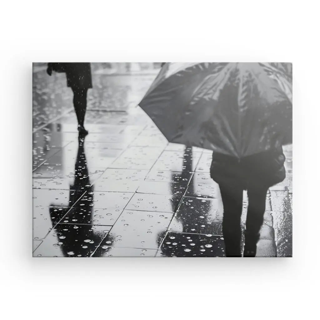 Une photo en noir et blanc capture une scène urbaine animée de gens marchant sur un trottoir mouillé sous la pluie. Une personne tient un parapluie, tandis que le sol reflète ses silhouettes et ses gouttelettes de pluie, créant ainsi un superbe Tableau Pluie Parapluie Scène Urbaine Noir et Blanc.