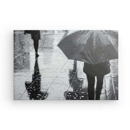 Photo en noir et blanc de personnes marchant sur un trottoir mouillé et réfléchissant sous la pluie, une personne tenant un parapluie. Ce saisissant Tableau Pluie Parapluie Scène Urbaine Noir et Blanc capture une scène urbaine poignante avec des détails remarquables.