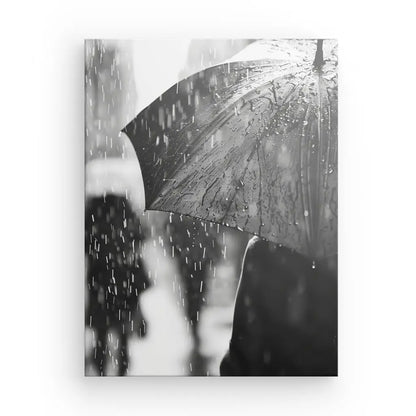 Photo en noir et blanc montrant une personne tenant un parapluie sous la pluie. Les gouttelettes d'eau tombent et s'accumulent visiblement sur la surface du parapluie. D'autres figures floues sont en arrière-plan, créant un Tableau Pluie Noir et Blanc évocatrice d'une scène pluvieuse.