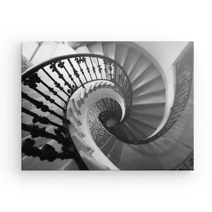 Photo en noir et blanc d'un escalier en colimaçon doté de rampes métalliques ornées, vu du dessus, mettant en valeur le motif géométrique des marches. Cette Œuvre d'art, ou Tableau Escalier Spirale Noir et Blanc, capture l'élégance dans son esthétique Noir et Blanc.