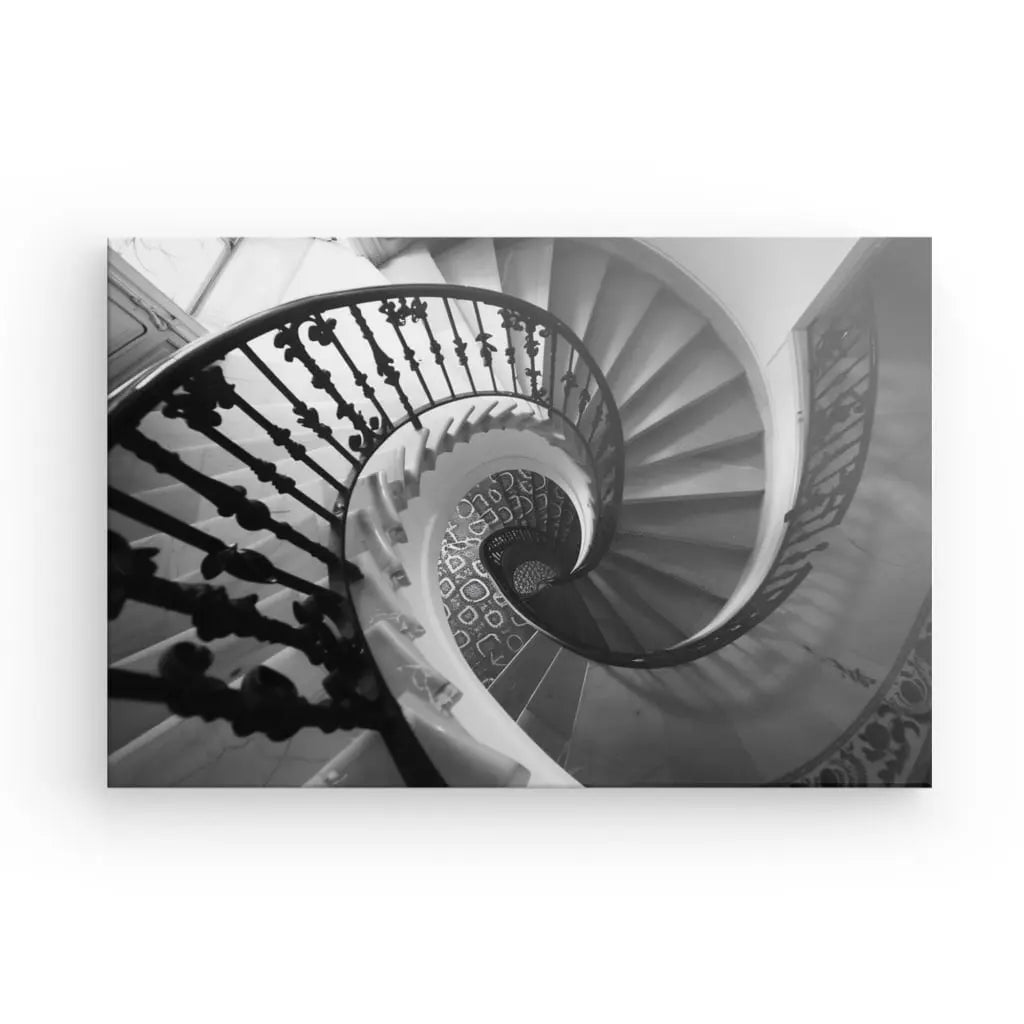 Une superbe image du Tableau Escalier Spirale Noir et Blanc d'un escalier en colimaçon, vu d'en haut. L'escalier se courbe dans un mouvement circulaire et les détails ornés de la balustrade le transforment en une œuvre d'art.