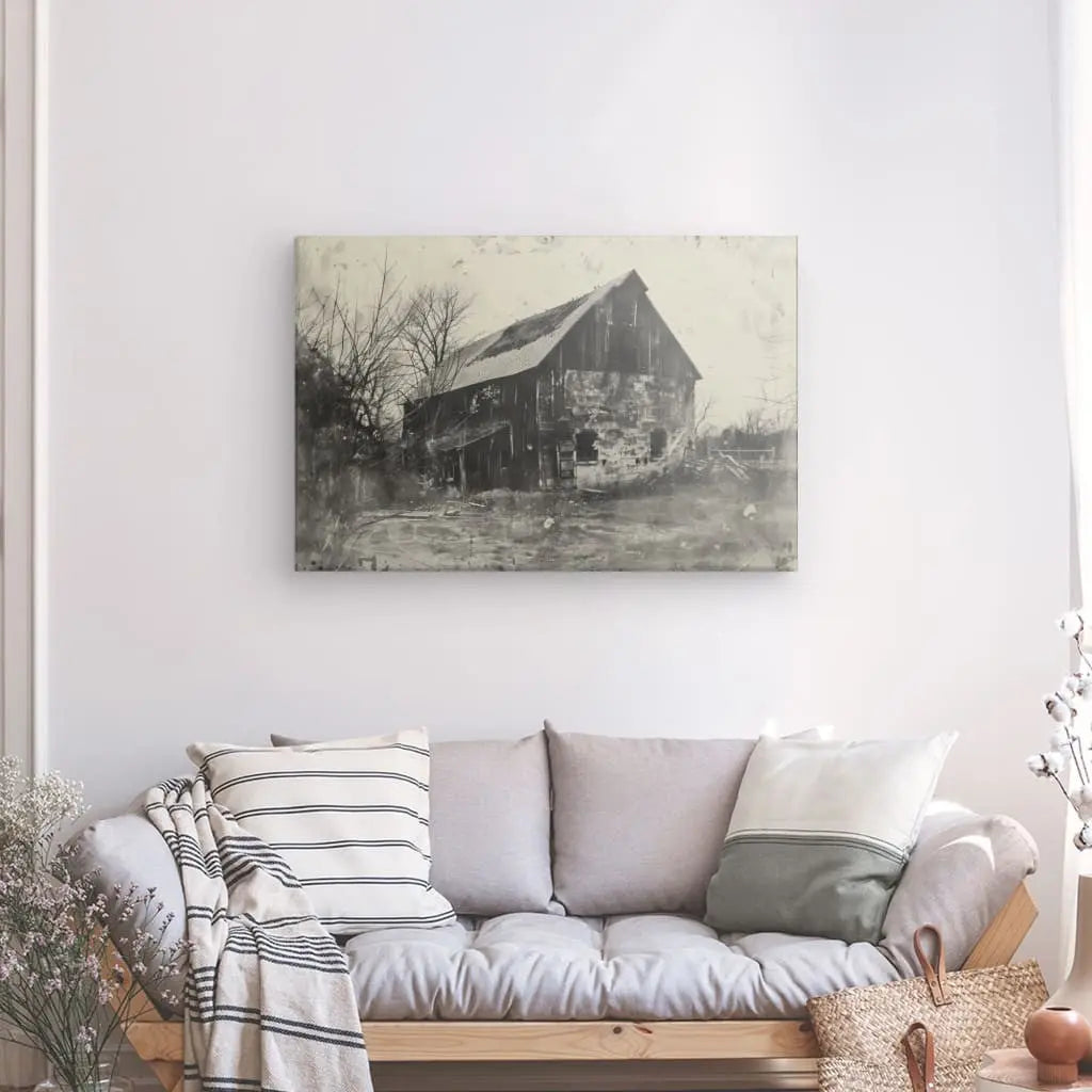 Un salon avec un canapé gris, des coussins rayés et unis, et un Tableau Grange Paysage Vintage Noir et Blanc d'une ancienne grange au mur. Un panier et des branches décoratives ajoutent au charme rustique, rehaussant l'atmosphère chaleureuse à côté du canapé.