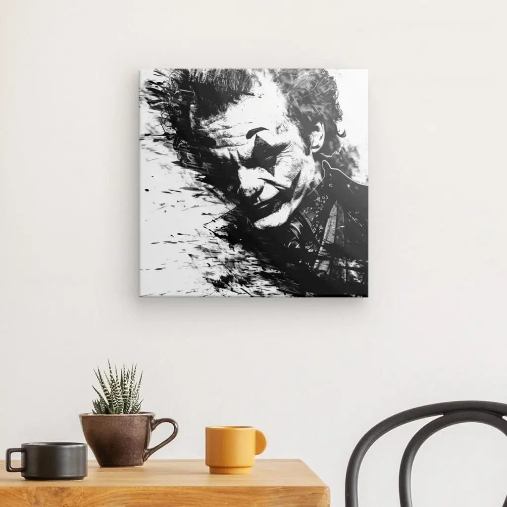 Un saisissant Tableau Joker Batman Portrait Noir et Blanc orne le mur, représentant un homme maquillé en clown. Ci-dessous, une table en bois contient une petite plante en pot à côté d'une tasse marron et d'une tasse jaune, complétées par une chaise noire dans cette élégante scène de décoration intérieure.