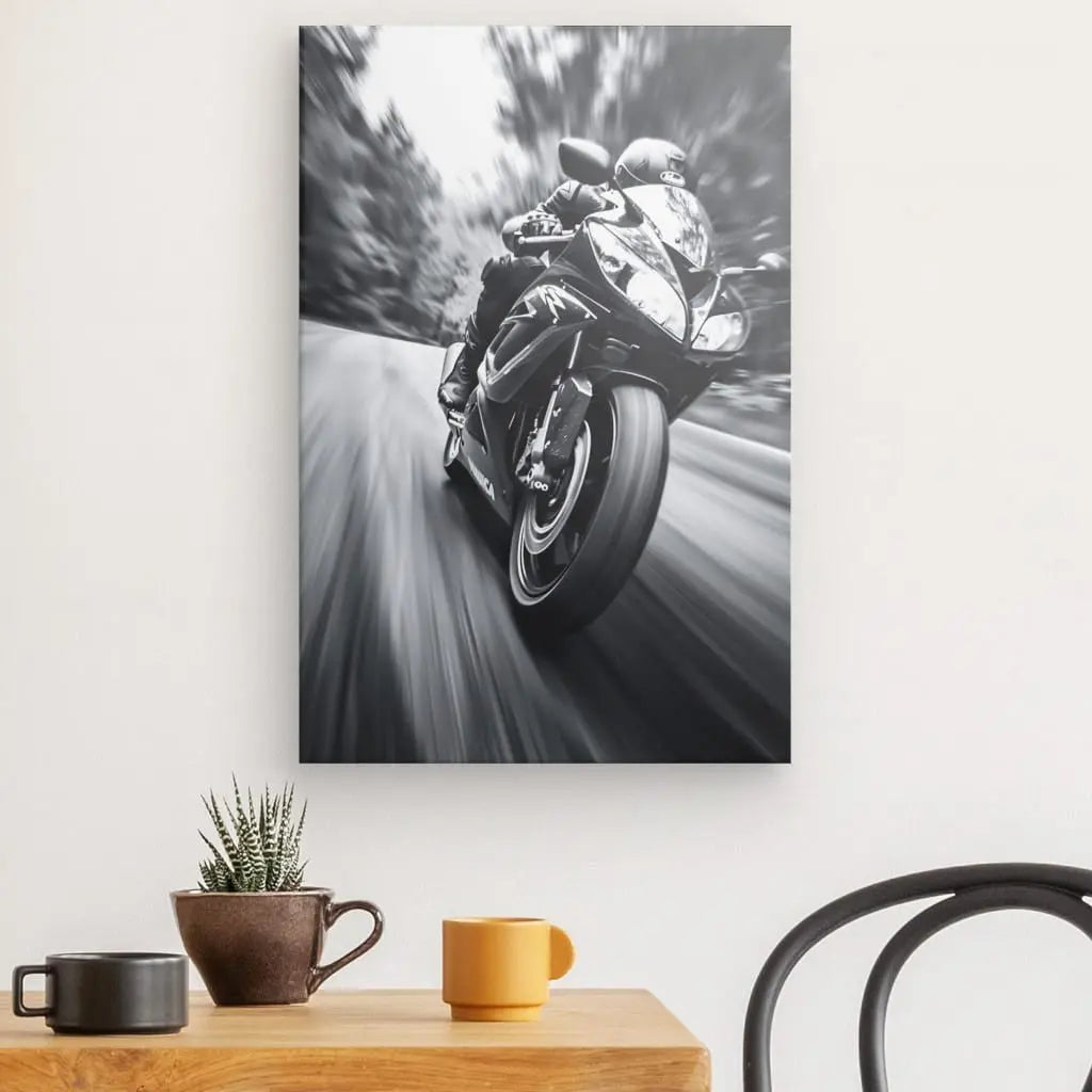 Un Tableau Moto Sport Photo Vitesse Noir et Blanc est monté sur un mur blanc au-dessus d'une petite table avec une plante en pot, une tasse marron et une tasse jaune, avec une chaise noire à proximité.