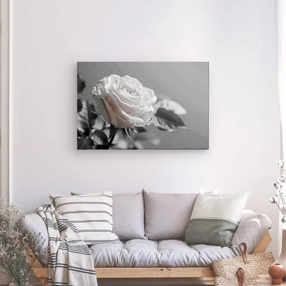 Un canapé gris avec plusieurs coussins est adossé à un mur blanc, orné d'une reproduction photo sur toile tendue à la main du Tableau Rose Fleur Délicate Noir et Blanc. Un panier et une petite table avec un vase de fleurs se trouvent au sol à proximité.