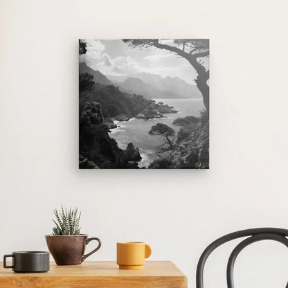 Une photographie en noir et blanc d'un paysage côtier avec des montagnes, imprimée à l'aide du Tableau Paysage Corse Noir et Blanc, accrochée sur un mur blanc au-dessus d'une table en bois avec une succulente en pot et deux tasses.