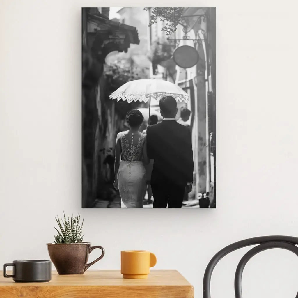 Une photo en noir et blanc au mur représente un couple marchant avec un parapluie, incarnant le Tableau Mariés Photo de Dos Ombrelle Noir et Blanc. Au premier plan, une table contient une tasse marron, une tasse jaune et une petite plante en pot. Une vue partielle d'une chaise est également visible.