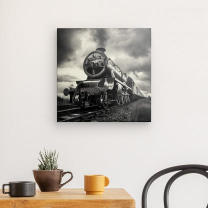 Le "Tableau Locomotive Vapeur Noir et Blanc" est accroché sur un mur blanc au-dessus d'une table en bois, ajoutant une touche de décoration industrielle. Sur la table se trouvent un pot marron avec une petite plante, une tasse marron et une tasse orange. Une chaise est partiellement visible.