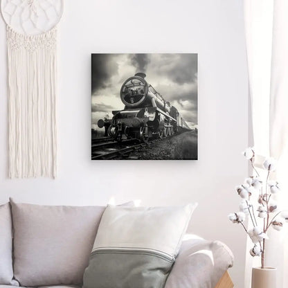 Dans un salon au mur blanc, le Tableau Locomotive Vapeur Noir et Blanc est exposé au-dessus d'un canapé gris orné de coussins crème et gris, créant un tableau industriel. Un décor tissé suspendu se trouve sur le mur de gauche.