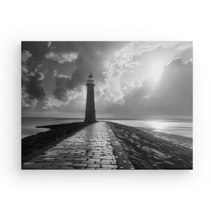 Photographie artistique en noir et blanc d'un phare au bout d'un chemin pavé, avec des nuages spectaculaires et la lumière du soleil perçant en arrière-plan. Parfait pour la décoration marine, ce Tableau Jetée Océan Phare Noir et Blanc capture la beauté éthérée des paysages côtiers.