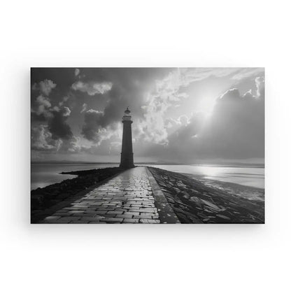 Un Tableau Jetée Océan Phare Noir et Blanc capture un phare au bout d'un chemin pavé, s'étendant dans l'océan sous un ciel nuageux. La lumière du soleil traverse les nuages, ajoutant à l'atmosphère dramatique de cette photographie artistique et à la décoration marine parfaite pour n'importe quel espace.