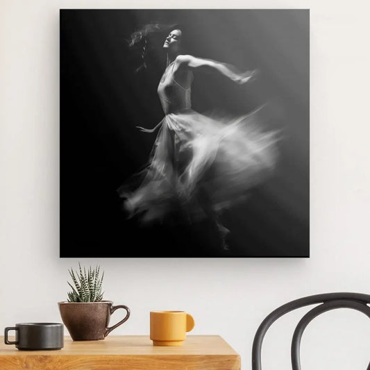 Art mural en noir et blanc, un Tableau Danseuse Robe Blanche Fond Noir représentant une danseuse de ballet en mouvement. Ci-dessous se trouve une table en bois avec deux tasses et une petite plante en pot, ajoutant à la décoration artistique. Une chaise noire est partiellement visible à droite.