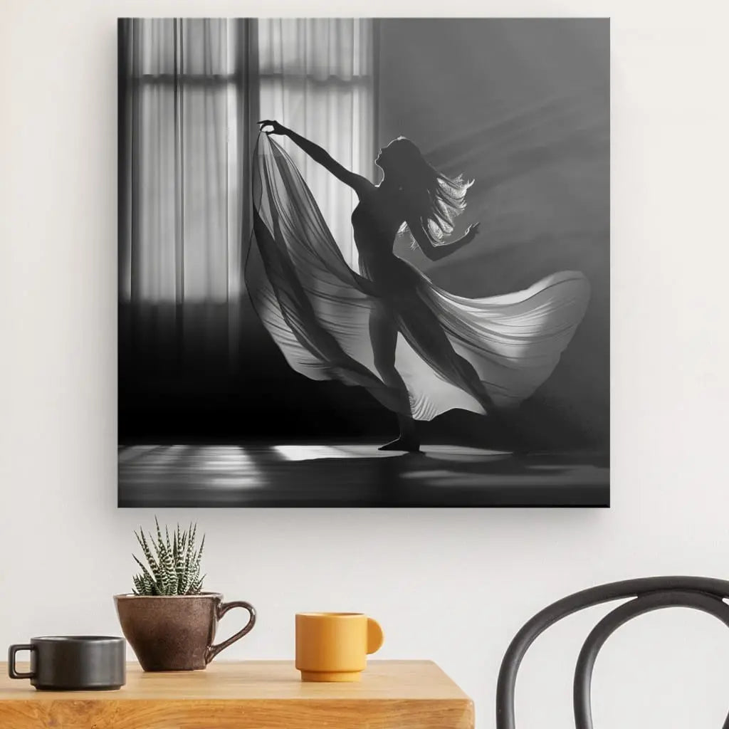 Photo en noir et blanc d'une danseuse en plein mouvement avec un tissu fluide. Ce Tableau Femme Voilage Robe Scène Noir et Blanc est exposé au-dessus d'une table en bois avec une petite plante et des tasses, créant un point focal artistique fascinant dans la pièce.