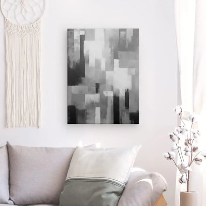 Un Tableau Peinture Abstraite Dégradé Noir et Blanc est suspendu au-dessus d'un canapé gris avec un oreiller, rehaussant la décoration moderne. A proximité, une tenture murale en macramé et un vase aux branches de coton complètent l'espace.