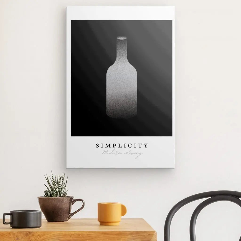 Le Tableau Bouteille Design "Simplicity" Noir et Blanc présente une illustration minimaliste d'une bouteille en niveaux de gris sur une toile murale. Ci-dessous, une table en bois contient une petite plante en pot et deux tasses, avec une partie d'une chaise noire visible à côté. Ce tableau noir et blanc ajoute un air de décoration sophistiquée à la scène.