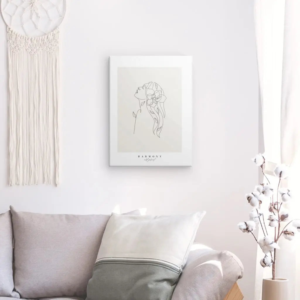 Salon minimaliste avec un canapé gris, une décoration murale blanche représentant un dessin au trait d'une femme, une pièce de macramé suspendue et un vase avec des tiges de coton, créant un Tableau "Harmonie" Beige Noir et Blanc qui incarne une décoration intérieure sophistiquée.