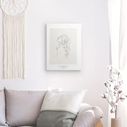 Salon minimaliste avec un canapé gris, une décoration murale blanche représentant un dessin au trait d'une femme, une pièce de macramé suspendue et un vase avec des tiges de coton, créant un Tableau "Harmonie" Beige Noir et Blanc qui incarne une décoration intérieure sophistiquée.