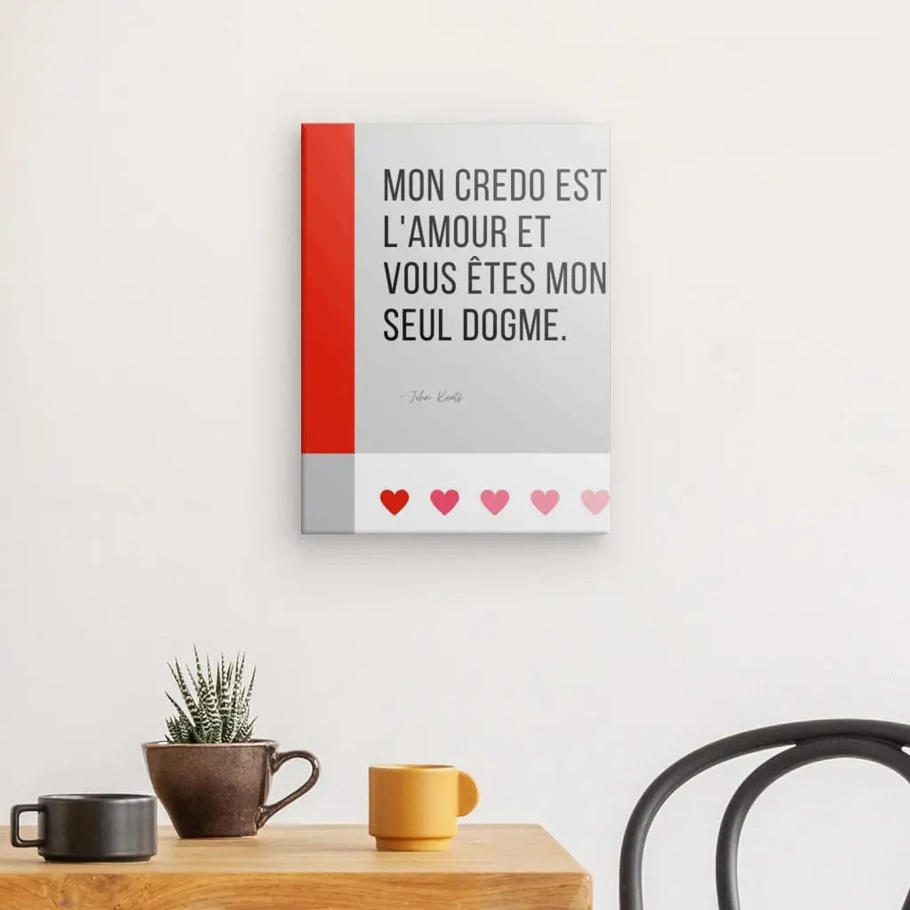 Un Tableau Citation Amour et Dogme Noir et Blanc mural avec une citation en français indique : « Mon credo est l'amour et vous êtes mon seul dogme ». Ci-dessous se trouve une table avec une plante dans un pot et deux tasses. Une vue partielle d'une chaise est à droite, créant une élégante ambiance noir et blanc.