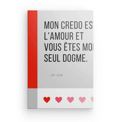 Une citation française de John Keats en texte noir sur un fond au thème noir et blanc avec une rangée de cinq cœurs en bas. On y lit : « Mon credo est l'amour et vous êtes mon seul dogme ». Ceci est représenté sur le produit Tableau Citation Amour et Dogme Noir et Blanc.