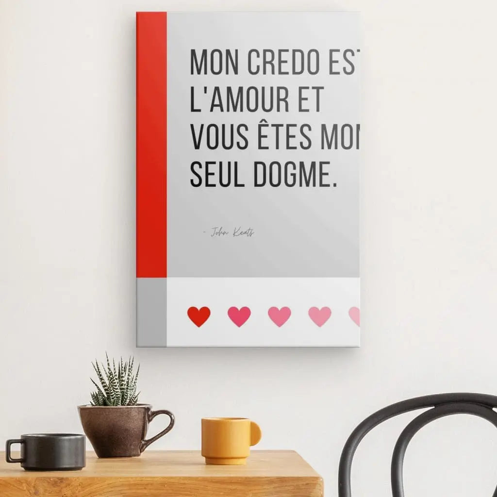 Un Tableau Citation Amour et Dogme Noir et Blanc comportant un texte français qui se traduit par « Mon credo est l'amour et tu es mon seul dogme » est accroché au-dessus d'une table en bois clair avec une plante en pot, une tasse orange et une tasse noire. Cette pièce fusionne art et philosophie dans un élégant design noir et blanc.