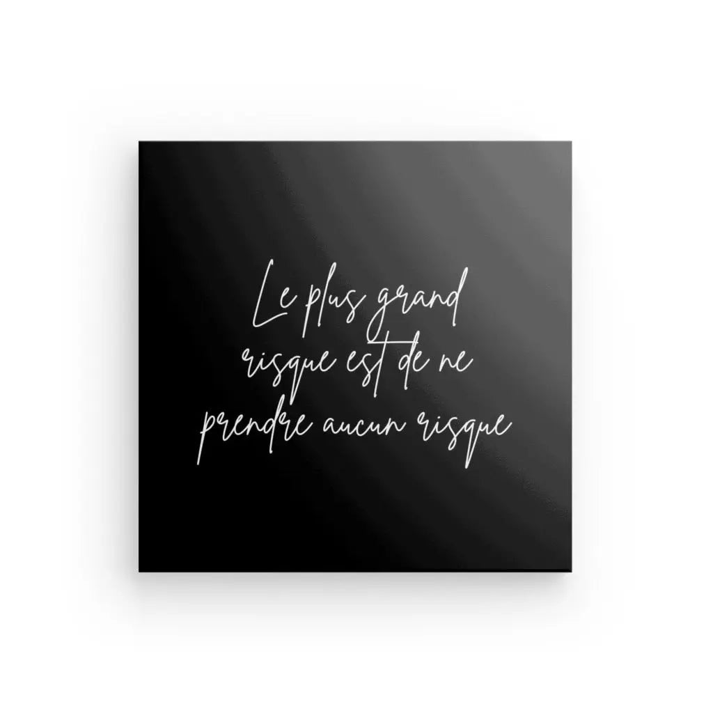 Une plaque d'inspiration au design minimaliste en noir et blanc comportant un texte cursif blanc qui dit : « Le plus grand risque est de ne prendre aucun risque » (« Le plus grand risque est de ne prendre aucun risque ») est connue sous le nom de Tableau Citation Risque Noir et Blanc.