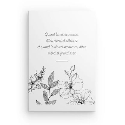 Un **Tableau Citation Fleurs et Gratitude Inversé** comportant une illustration florale en noir et blanc et un texte en français qui dit : "Quand la vie est douce, dites merci et célèbrez et quand la vie est meilleure, dites merci et grandissez", parfait pour une décoration intérieure élégante.