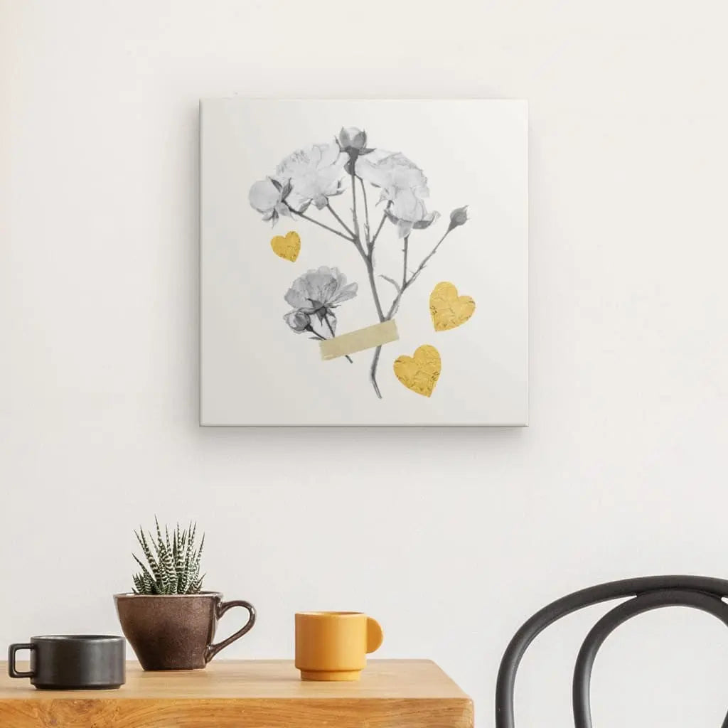 Une impression d'art mural, Tableau Fleurs Séchées Monochrome Coeurs Jaunes, représentant des fleurs grises et des cœurs dorés, est accrochée au-dessus d'une table en bois avec une plante en pot et deux tasses à café. La scène, présentant une décoration intérieure impressionnante, est complétée par une chaise noire au premier plan à droite.