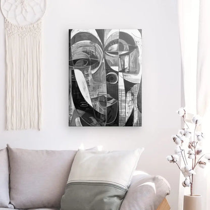 Un salon comprend un canapé gris avec des coussins blancs et gris, une tenture murale tissée et un Tableau Cubisme Visage Abstrait Noir et Blanc au-dessus du canapé. Des tiges de coton dans un vase sont placées à côté du canapé, ajoutant à la décoration intérieure sophistiquée.